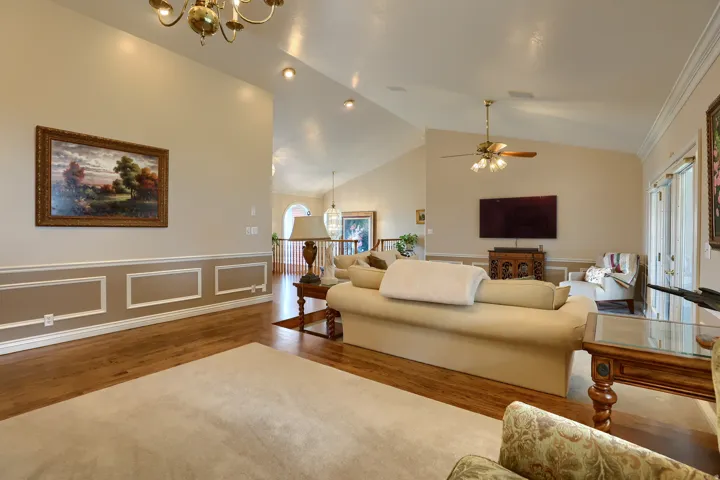 Living room featuring wood-finish flooring, vaulted ceilings, recessed lighting, and chair rail molding with decorative paneling