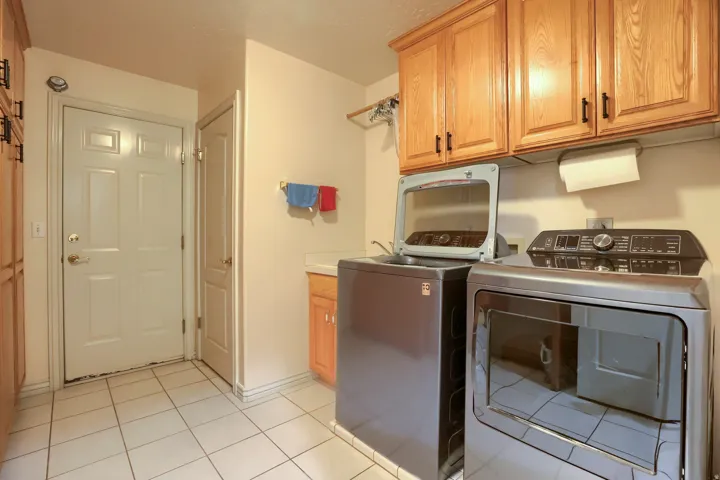 Laundry room featuring a white paneled door, tile flooring, and light wood cabinetry with dark hardware