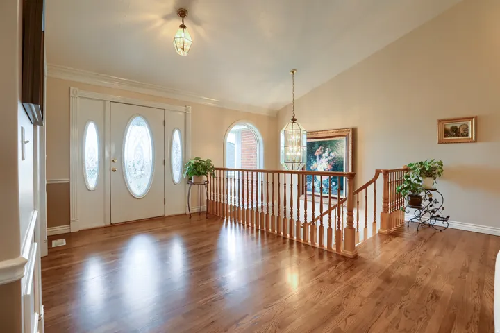 Double entry doors with decorative oval glass inserts, polished wood-finish flooring, a wood banister, a vaulted ceiling, and an arched window