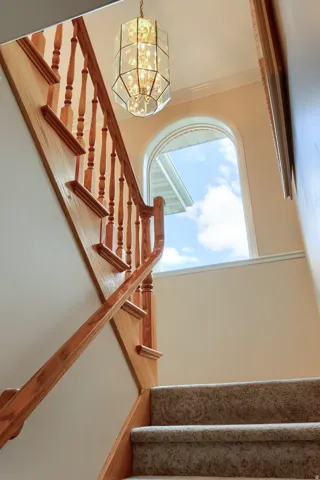 Carpeted staircase with light wood banister and spindles, illuminated by a decorative glass chandelier