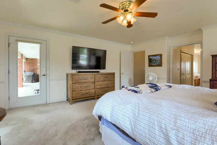 Carpeted room featuring a ceiling fan with integrated lighting, crown molding, and a paneled door leading to an outdoor area with brickwork