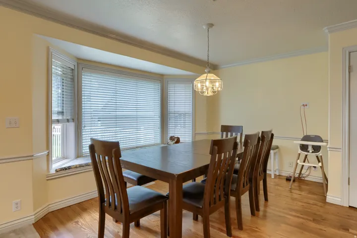 Dining area featuring a bay window, hardwood flooring, a ceiling-mounted chandelier, and crown molding