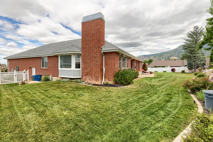 Expansive lawn area featuring a paved patio, red brick exterior, bay window, and surrounding landscaping