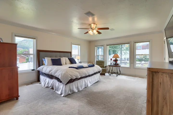 Spacious room featuring neutral carpet flooring, multiple windows, a ceiling fan with integrated lighting, and crown molding