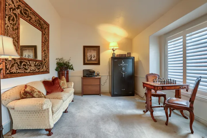 Carpeted room with a vaulted ceiling, featuring plantation shutters on a large window, decorative crown molding, and a built-in safe