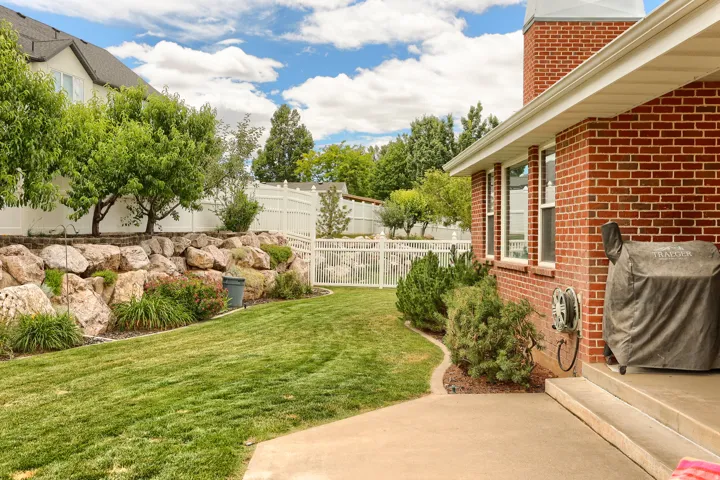 Expansive backyard featuring a manicured lawn, a rock retaining wall, mature trees, and a white privacy fence