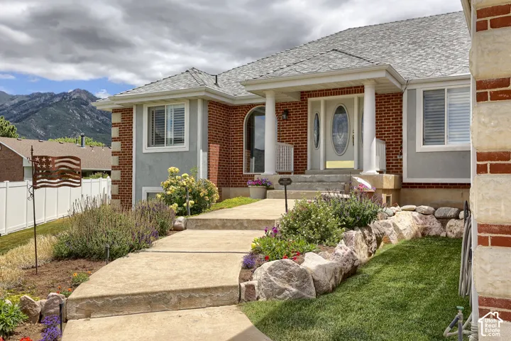 Brick and stucco exterior featuring a columned entryway, arched transom window, and a gray shingle roof