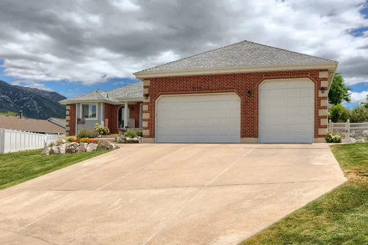 Brick exterior with a three-car garage, concrete driveway, and front landscaping featuring rockery and plantings