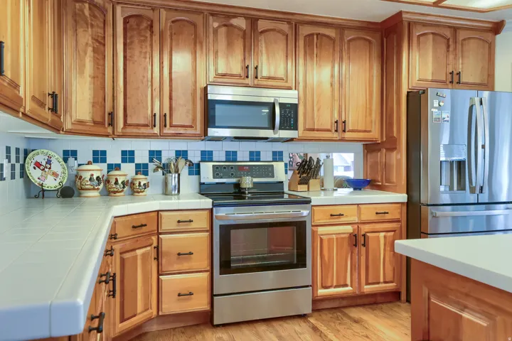 Kitchen featuring wood cabinetry, stainless steel appliances, tile countertops, a tiled backsplash, and wood-finish flooring