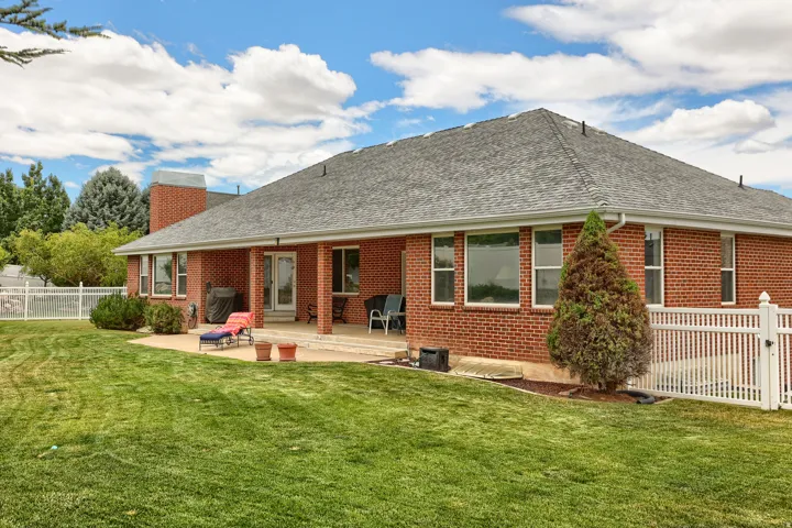Expansive green lawn bordering a brick exterior with a covered patio area, featuring multiple windows and a white picket fence