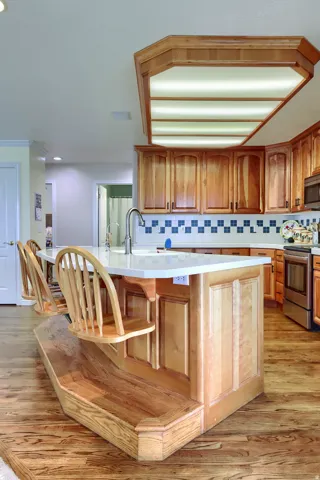 Kitchen featuring a large central island with integrated seating, light wood-finish cabinetry, a patterned tile backsplash, and a large tray ceiling light fixture