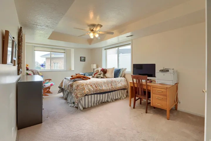 Bedroom featuring a tray ceiling with a ceiling fan, two large windows, carpet flooring, and neutral wall tones
