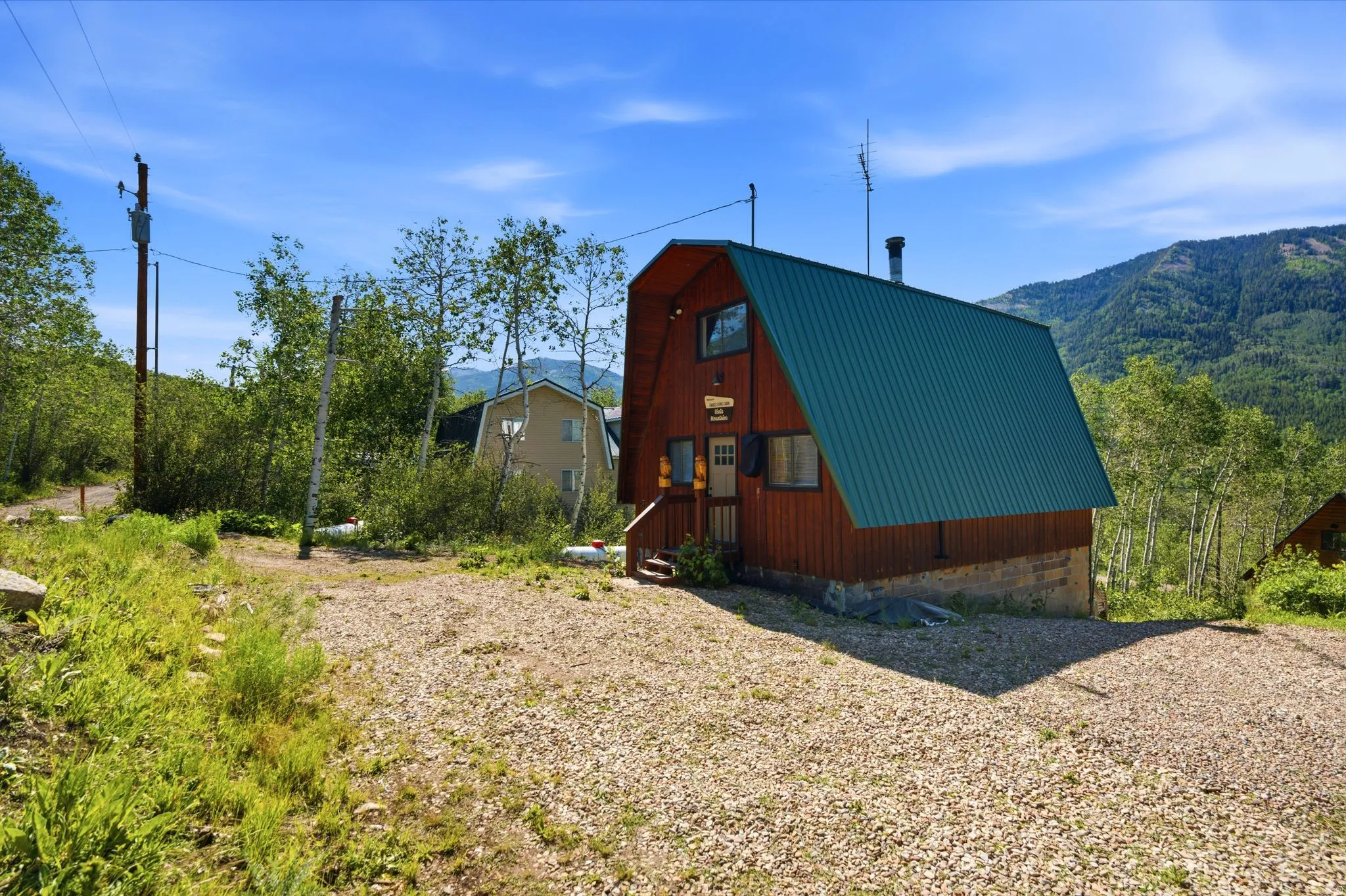 A-frame structure featuring wood siding, a green metal roof, and a gravel parking area