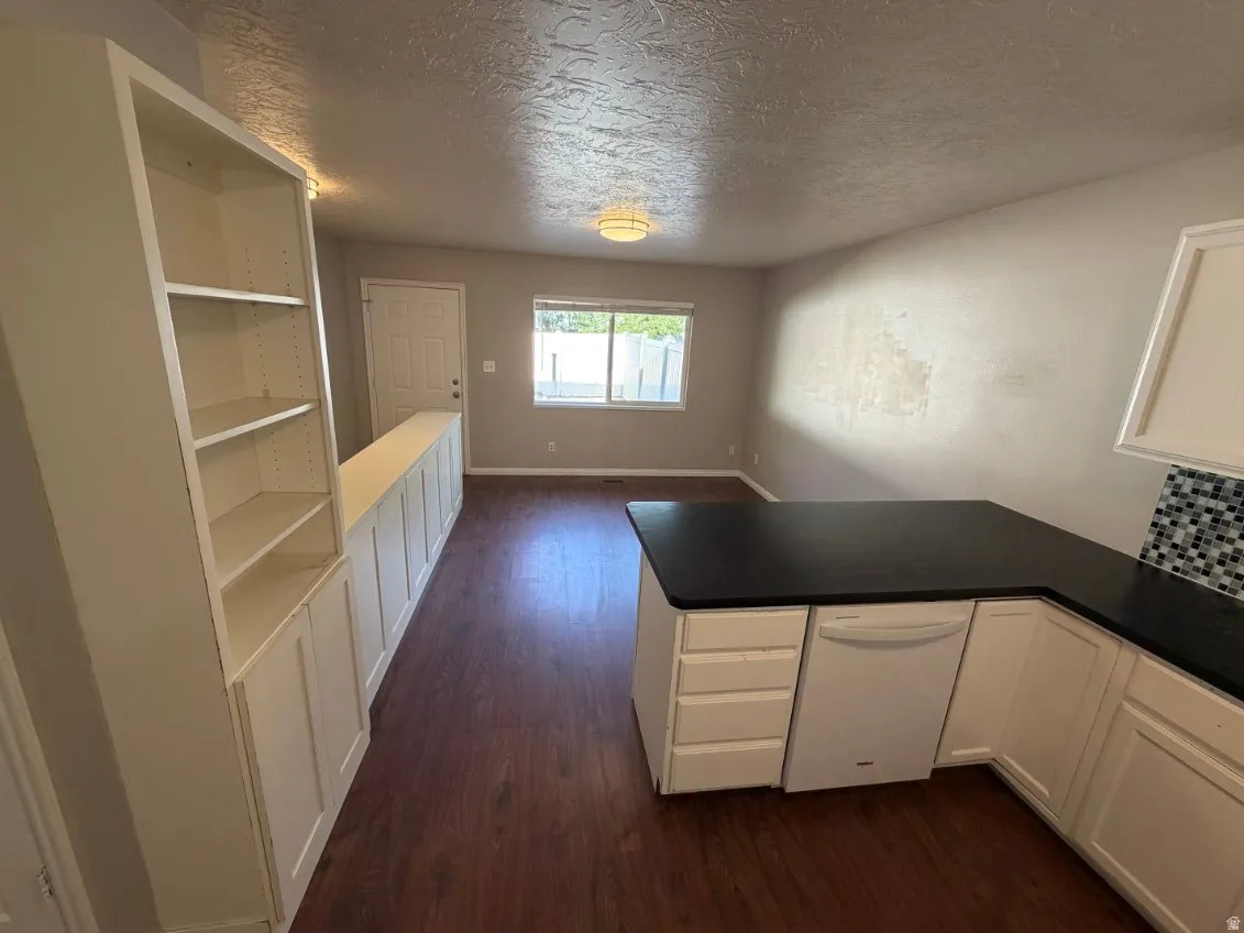 Kitchenette featuring a white dishwasher, L-shaped black countertop, and mosaic tile backsplash