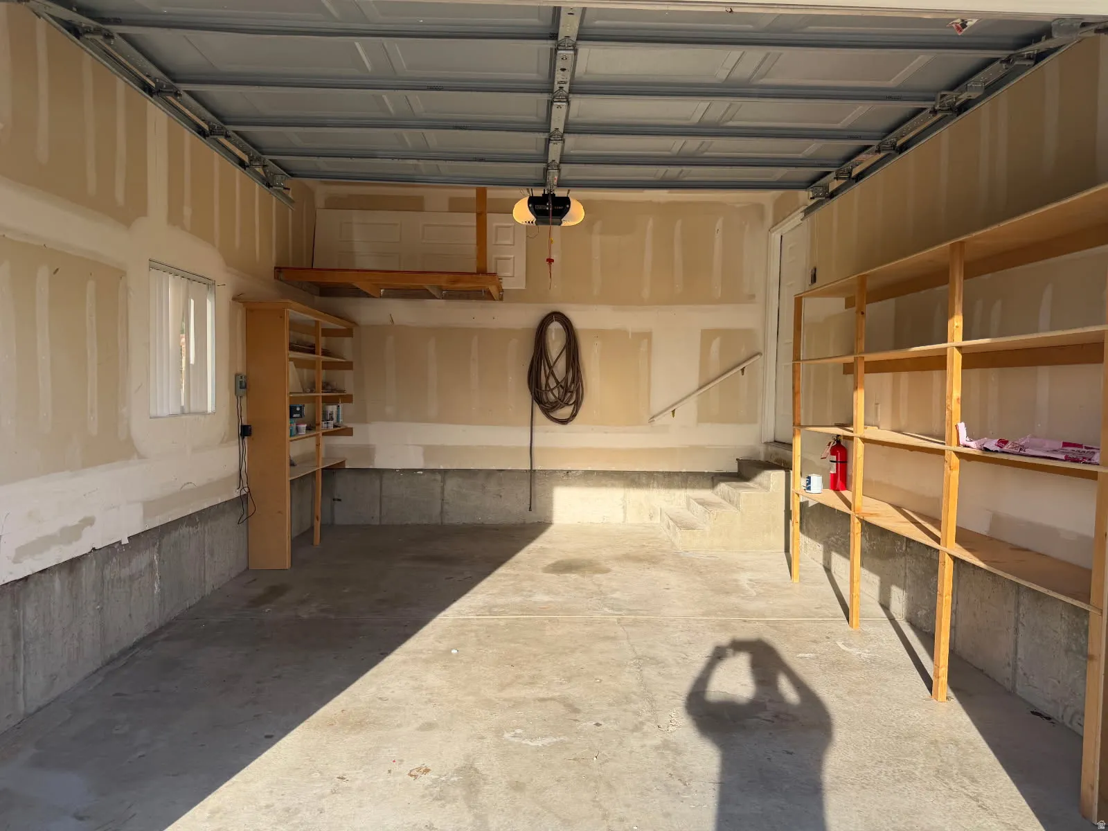 Spacious garage featuring a concrete floor, built-in shelving, an overhead storage platform, a window, and an automatic garage door opener
