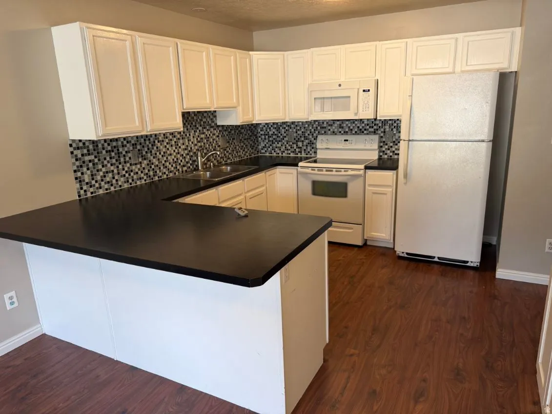 U-shaped kitchen featuring white cabinetry, dark countertops, a mosaic tile backsplash, and wood-finish flooring