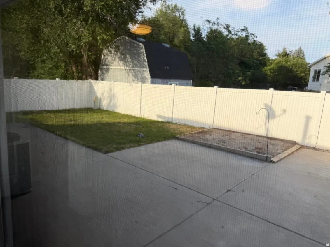 Private backyard featuring a white vinyl fence, concrete patio, and a dedicated garden bed