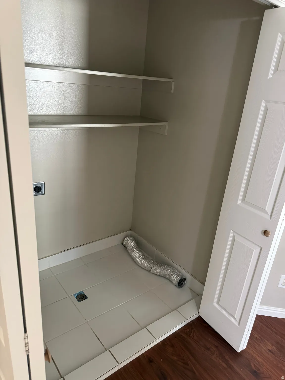 Utility closet with tiled flooring, two built-in shelves, electrical outlet, and a bi-fold door