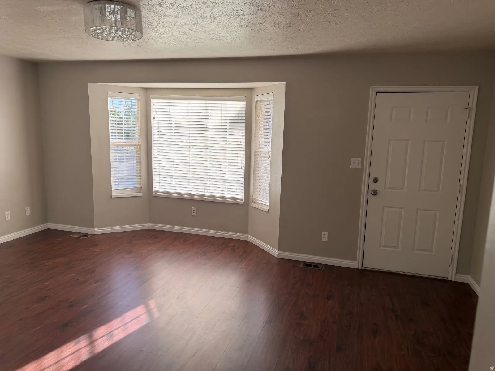 Living area featuring a bay window with blinds, wood-finish flooring, and a flush-mount ceiling light fixture