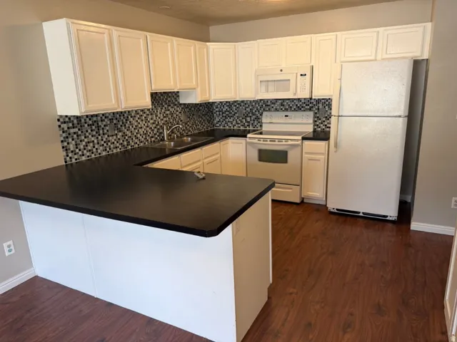 U-shaped kitchen featuring white cabinetry, dark countertops, a mosaic tile backsplash, and wood-finish flooring