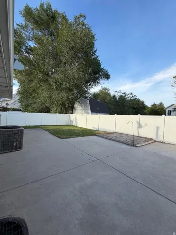 Rear concrete patio featuring a white privacy fence and a large mature tree