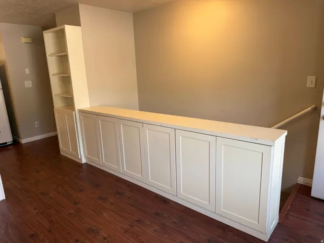 Built-in white cabinetry with a coordinating counter surface, integrated shelving, and wood-finish flooring