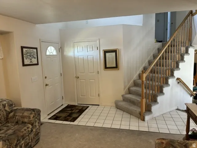 Entry foyer with neutral tile flooring, a carpeted staircase with wood banister, and two white paneled doors