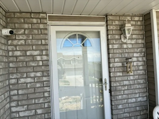 Exterior entry featuring brick facade, white storm door with arched window, and outdoor wall lantern