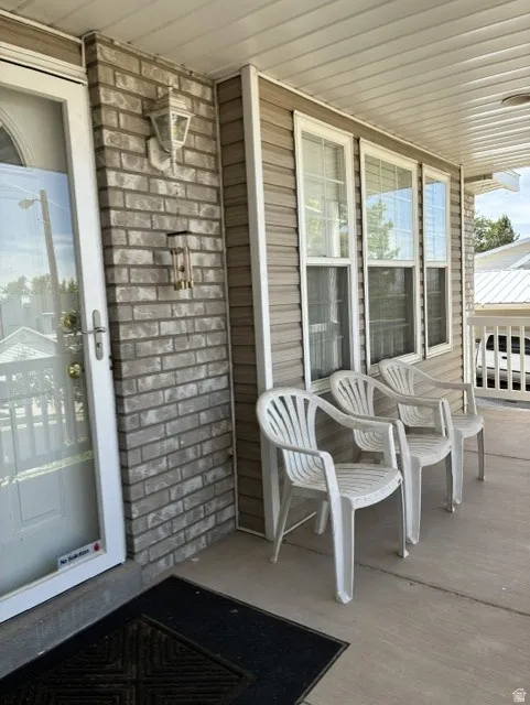 Covered front porch featuring a brick facade accent wall, tan horizontal siding, and multiple vertical windows
