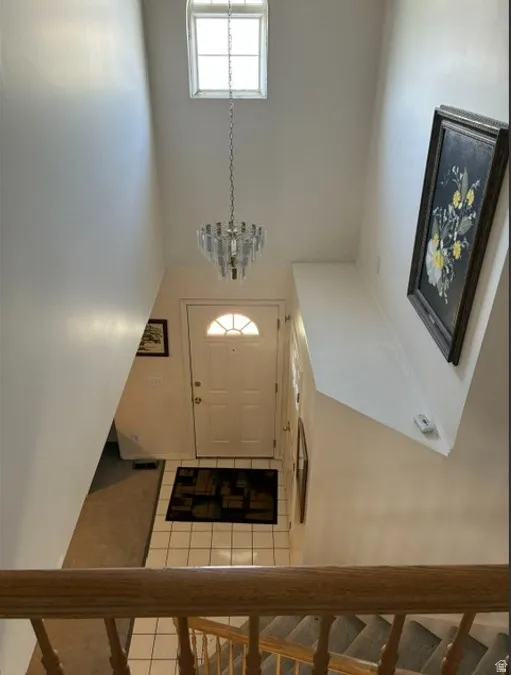 Entryway featuring a white paneled door with an arched glass insert, illuminated by a hanging chandelier and an overhead transom window
