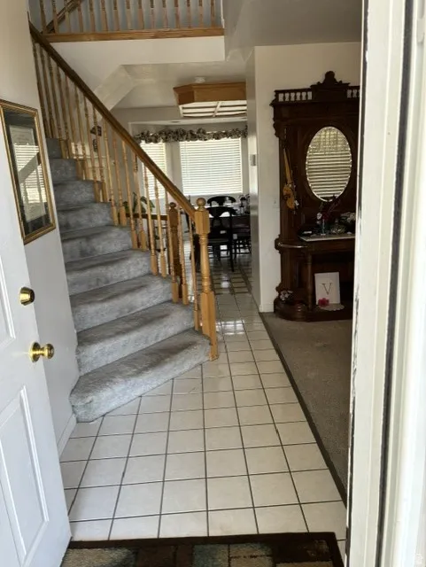 Entryway featuring light-colored square tile flooring and a carpeted staircase with a wood banister