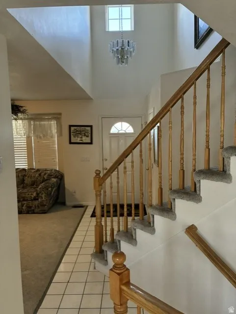 Two-story entry foyer featuring a chandelier, a transom window, tile flooring, and carpeted stairs with a wood baluster railing