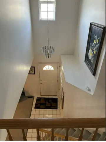 Bright foyer featuring a high ceiling with natural light from an upper window, elegant pendant chandelier, tile flooring, and paneled entry door with transom window detail