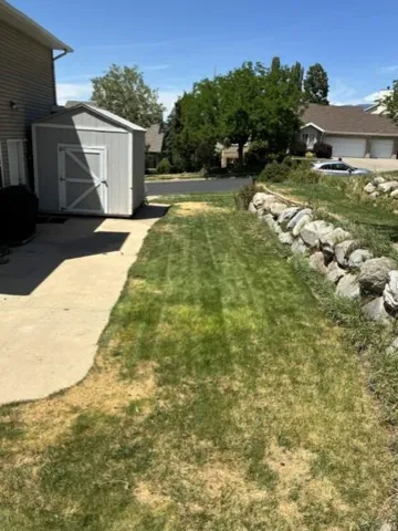 Storage shed, rock retaining wall, concrete patio, grass area, mature trees