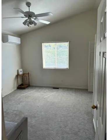 Vaulted ceiling with an attached ceiling fan, wall-mounted air conditioning unit, and a window with blinds
