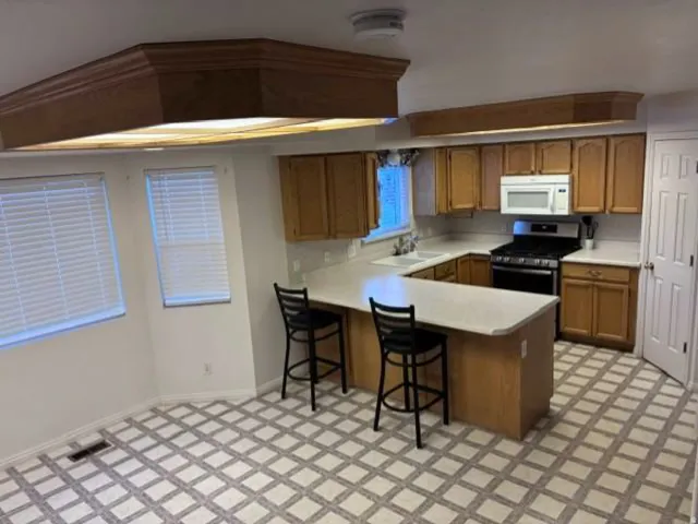 U-shaped kitchen featuring wood-finish cabinetry, a gas range, and a built-in microwave