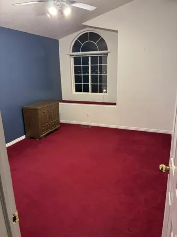 Arched window with gridded design, ceiling fan with integrated lighting, and red carpeting