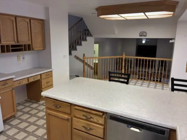 Kitchen featuring wood-finish cabinetry, light-toned countertops, and an integrated stainless steel dishwasher