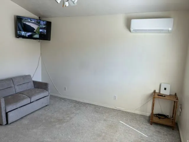 Carpeted room with a wall-mounted mini-split AC unit and an overhead ceiling fan