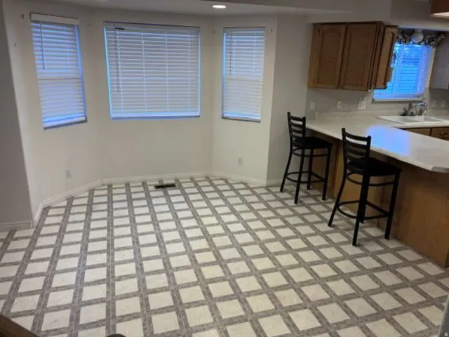 Bright dining area with bay windows, patterned flooring, and a breakfast bar with wood-finish cabinetry