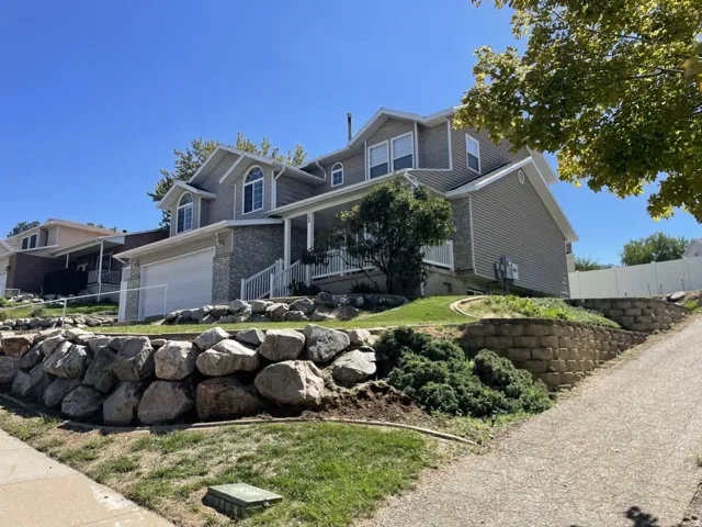 Two-story residence featuring a covered front porch, an attached garage, and a tiered rock retaining wall