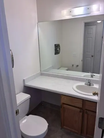 Bathroom featuring a wood-finish vanity with ample counter space, round ceramic sink, chrome faucet, and large mirror with overhead lighting