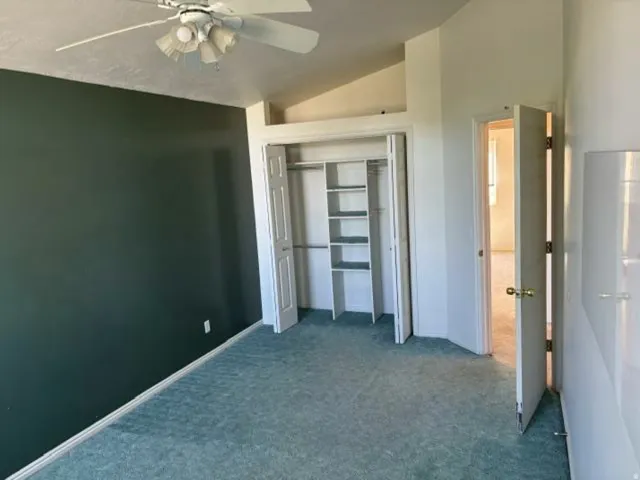 Spacious bedroom featuring neutral carpet flooring, a ceiling fan with integrated lighting, and a reach-in closet with shelving