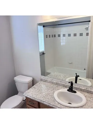 Bathroom featuring a vanity with a light-toned speckled countertop, an oval undermount sink with a black faucet, and a white tiled shower with decorative accent squares