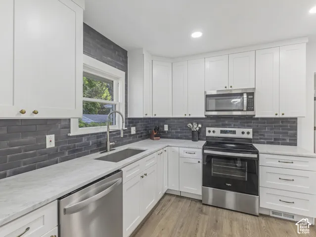 Home 2/2 - 938 E Herbert Avenue --Modern kitchen showcasing white cabinetry with brass hardware, stainless steel appliances, a deep basin sink with a gooseneck faucet, light-toned countertops, and a dark tile backsplash