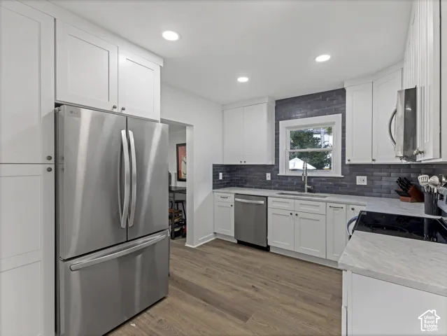 Home 2/2 - 938 E Herbert Avenue --Kitchen featuring white shaker-style cabinetry, stainless steel appliances, a dark subway tile backsplash, light-toned countertops, and wood-finish flooring