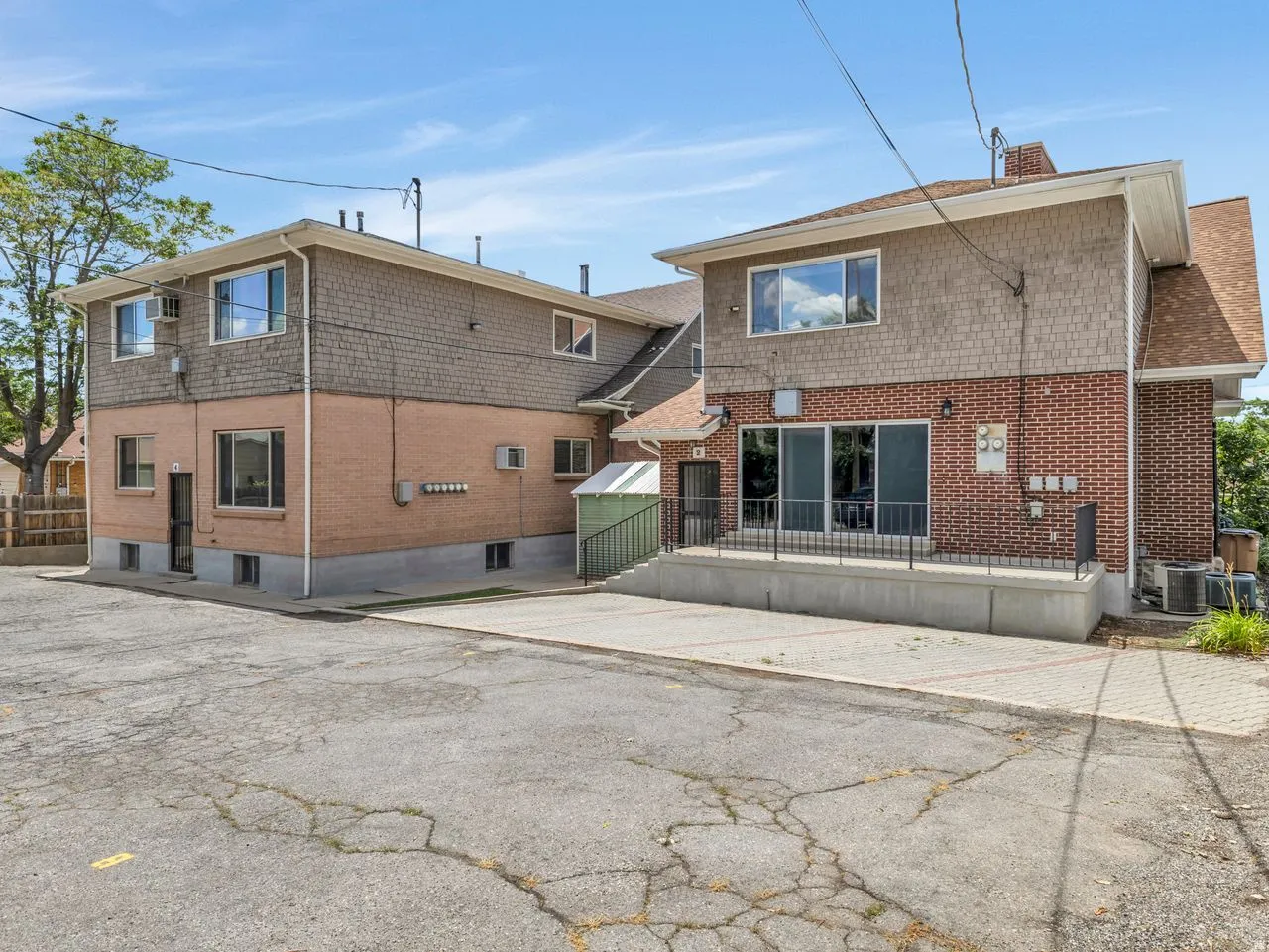 Two-story structure featuring brick and shake siding, multiple windows, a ground-level patio with black railings, and a lower-level entrance with a screened door