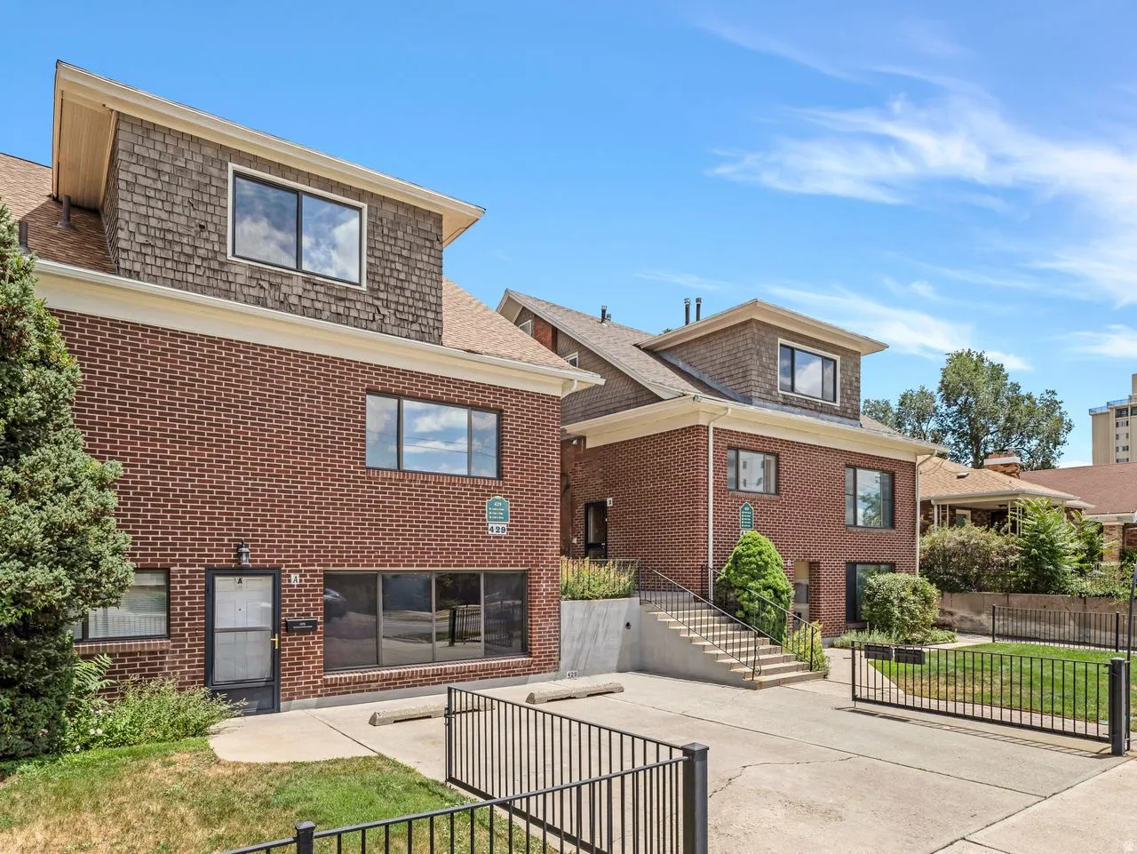 Brick facade structure featuring dormer windows with shingle siding, a gated entrance, and an exterior stairway
