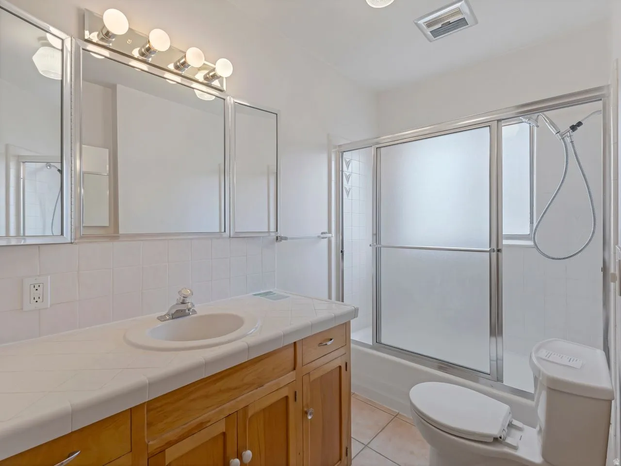 Bathroom featuring a light wood-finish vanity with an integrated sink, a white tiled countertop, and a chrome faucet