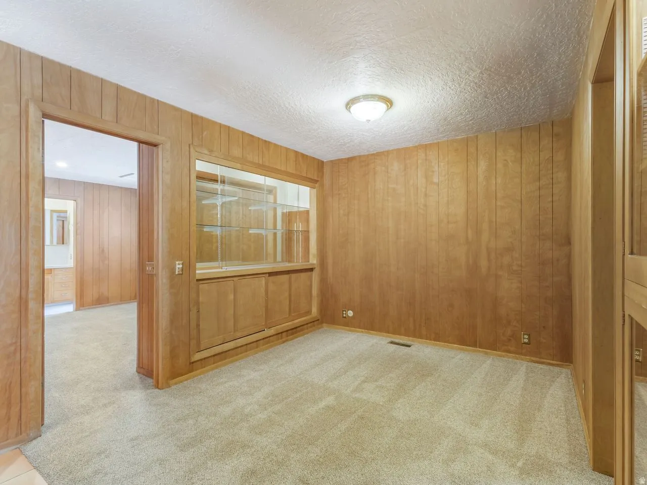 Interior room featuring wood paneling throughout, a built-in display cabinet with glass shelving and lower cabinetry, and textured ceiling